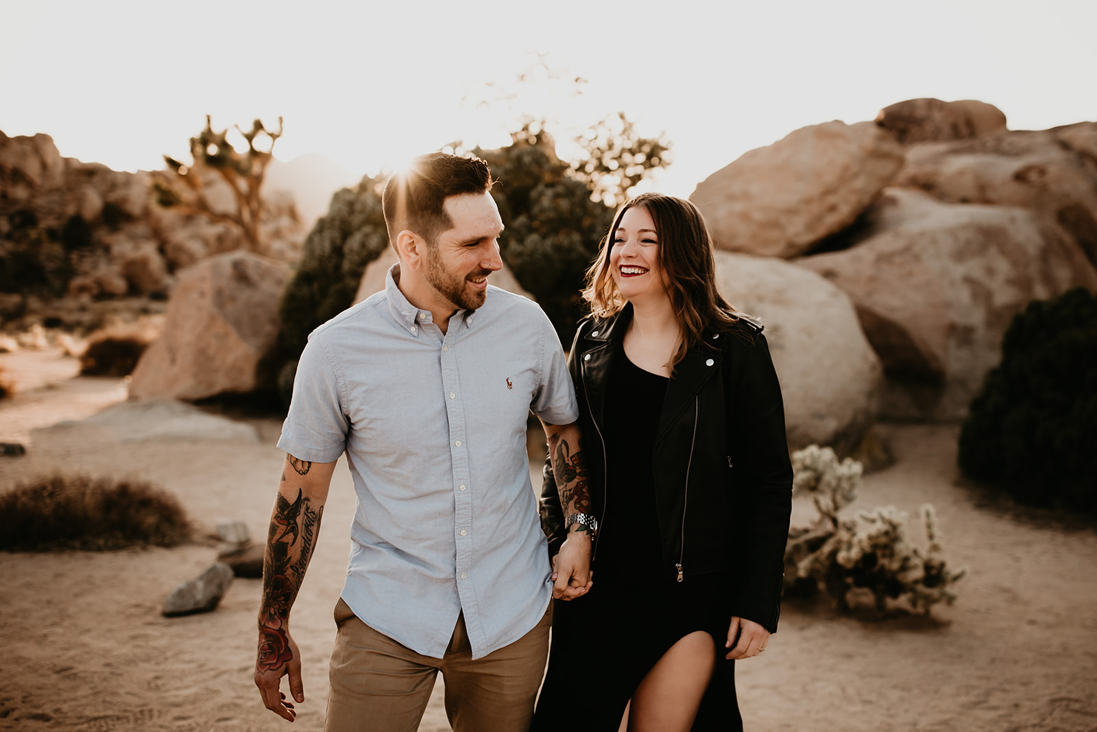 A couple smiling and walking through Joshua Tree National park for their engagement photos