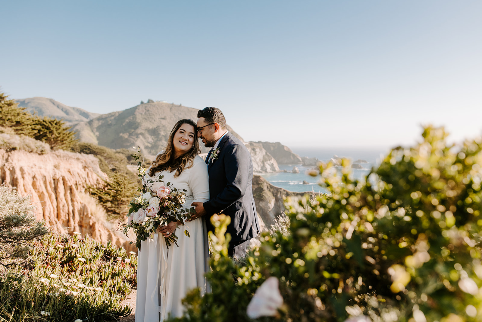 A couple who eloped in Big Sur, California embrace overlooking the coastline