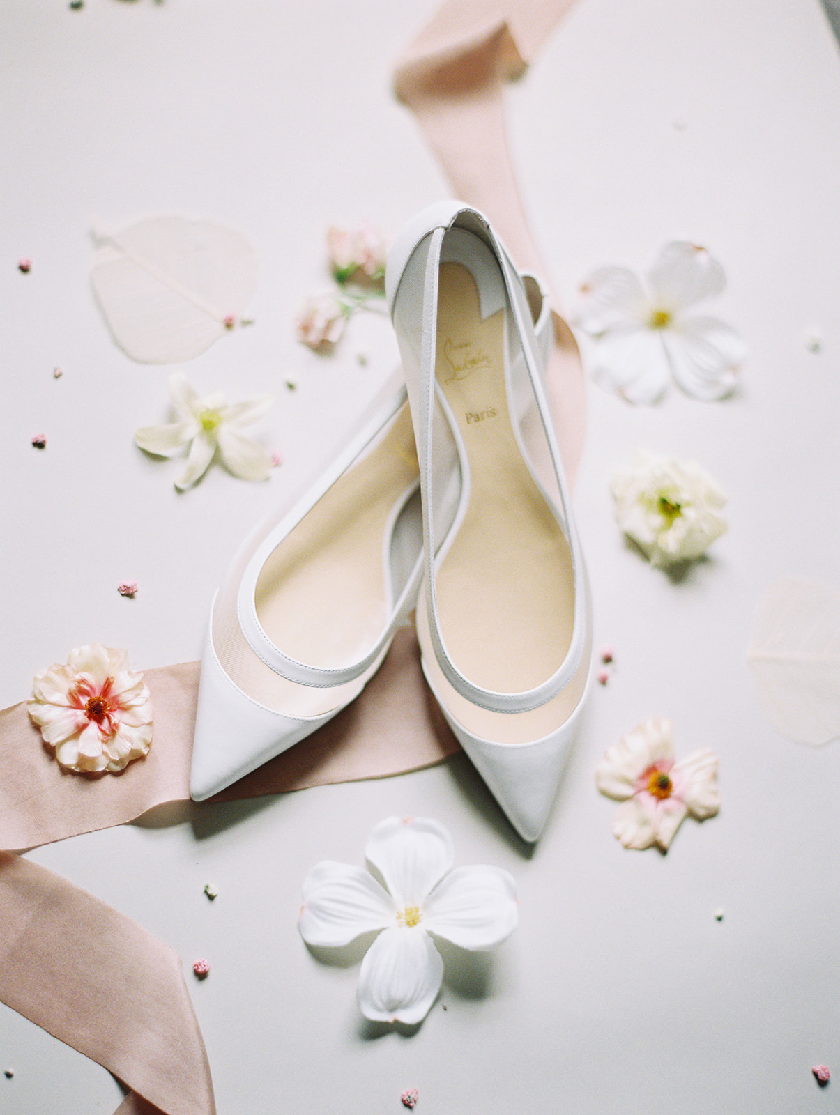 White Louboutin wedding flats surrounded by white and pink flowers