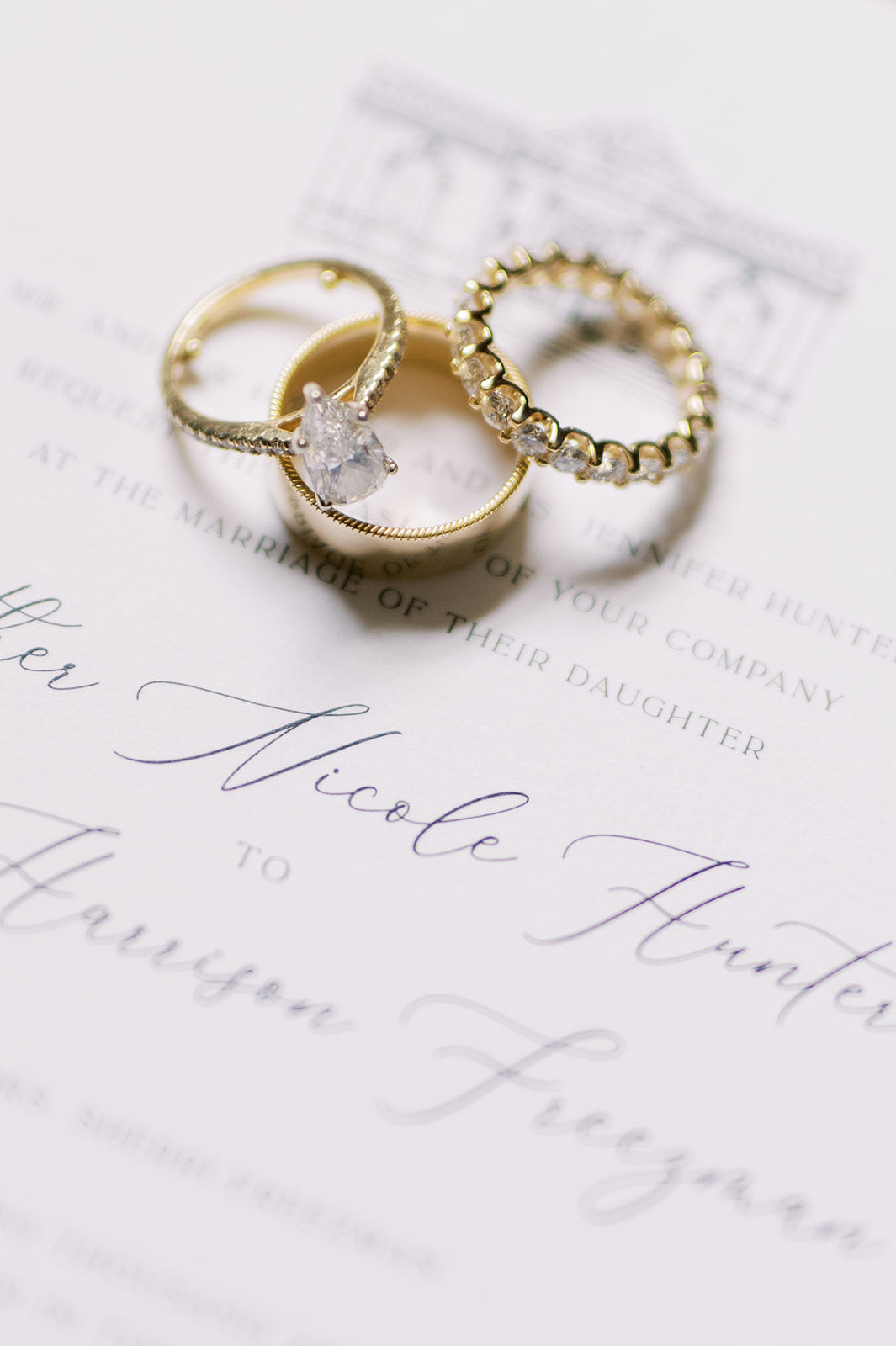 Engagement ring and wedding bands laid on invitation