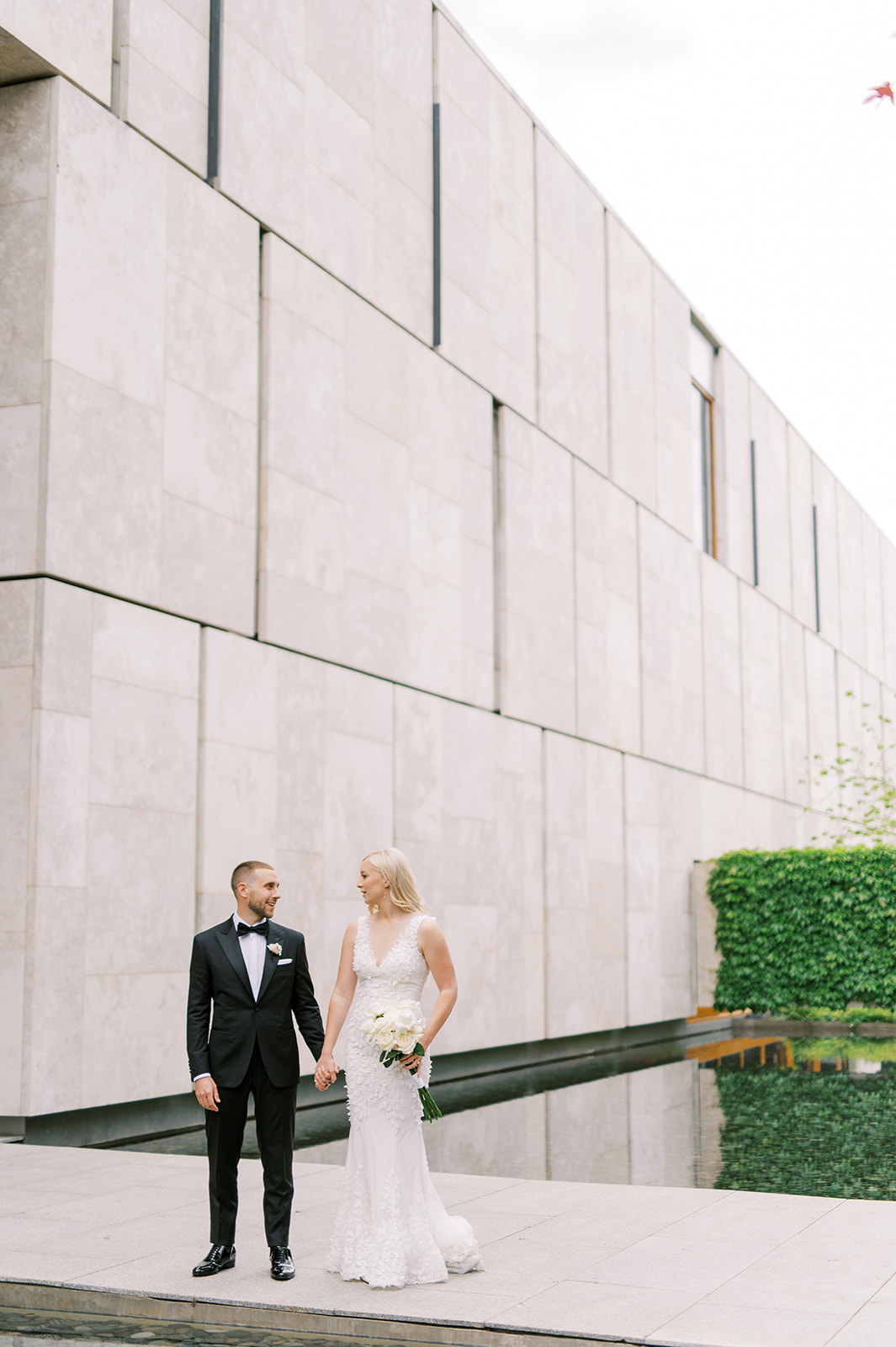 bride and groom holding hands against marble wall of Barnes Foundation