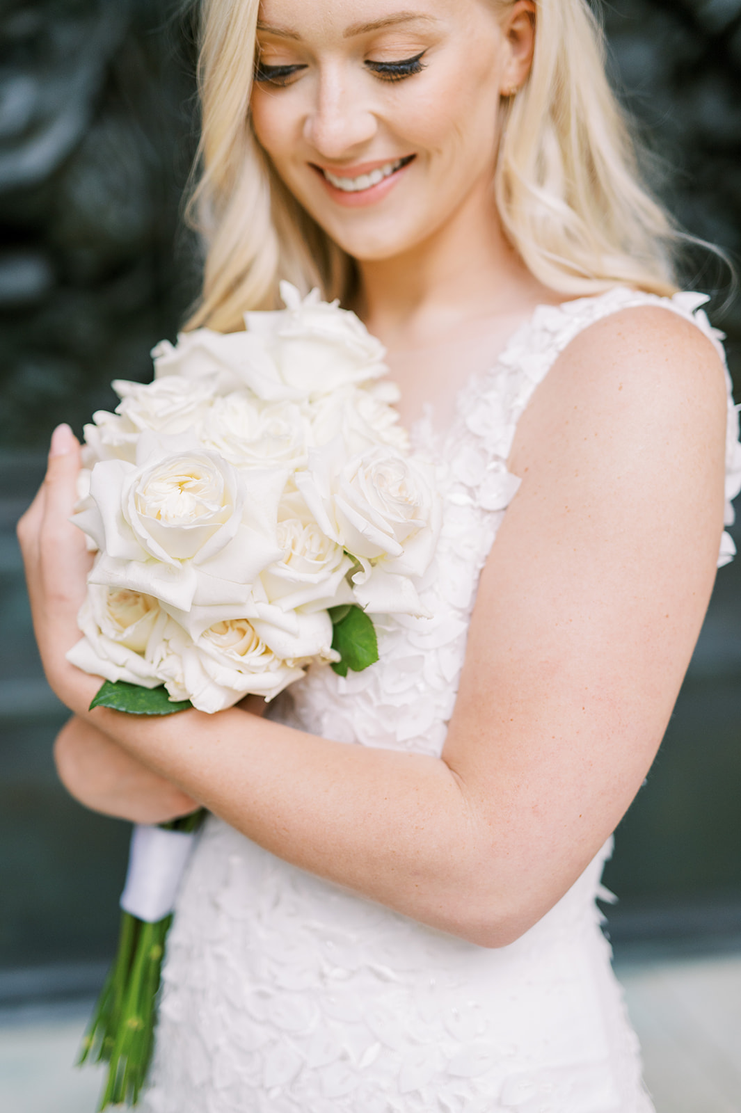bride looking down and smiling holding a bouquet of long-stem white roses 