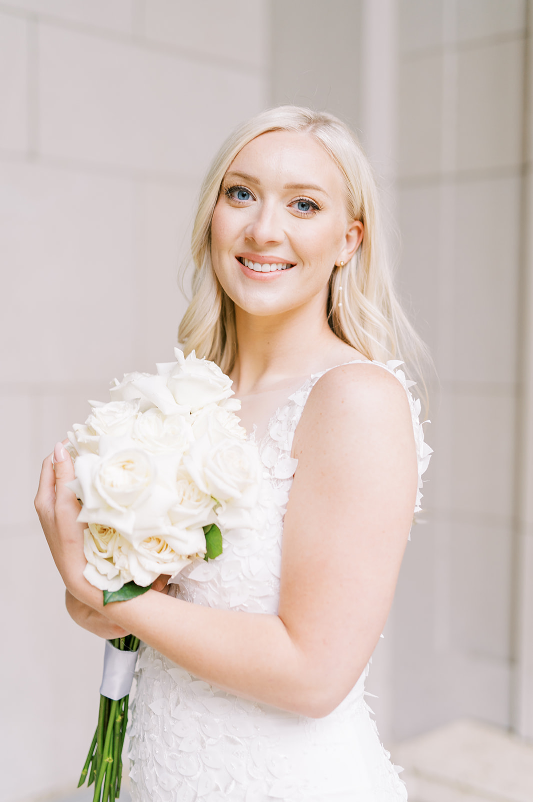 Bride smiling at camera holding bouquet of long-stem white roses