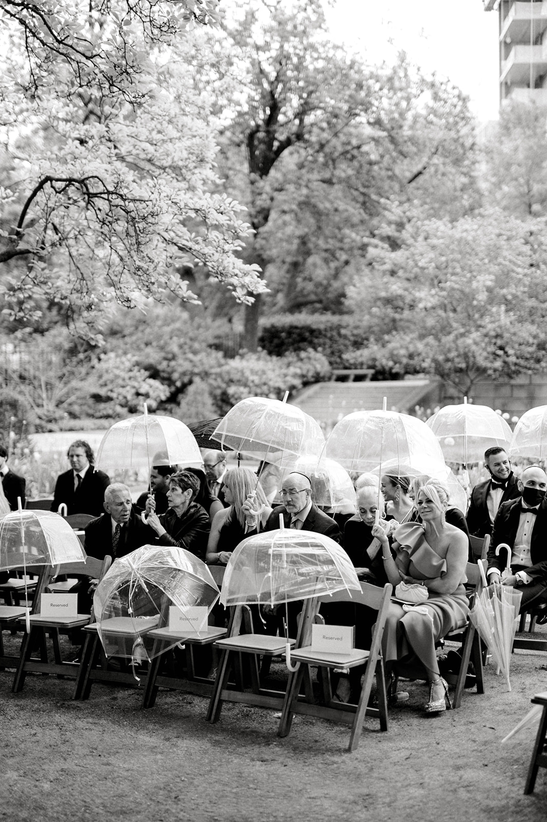 black and white photos of guests seated at the Rodin Museum for a ceremony holding umbrellas 