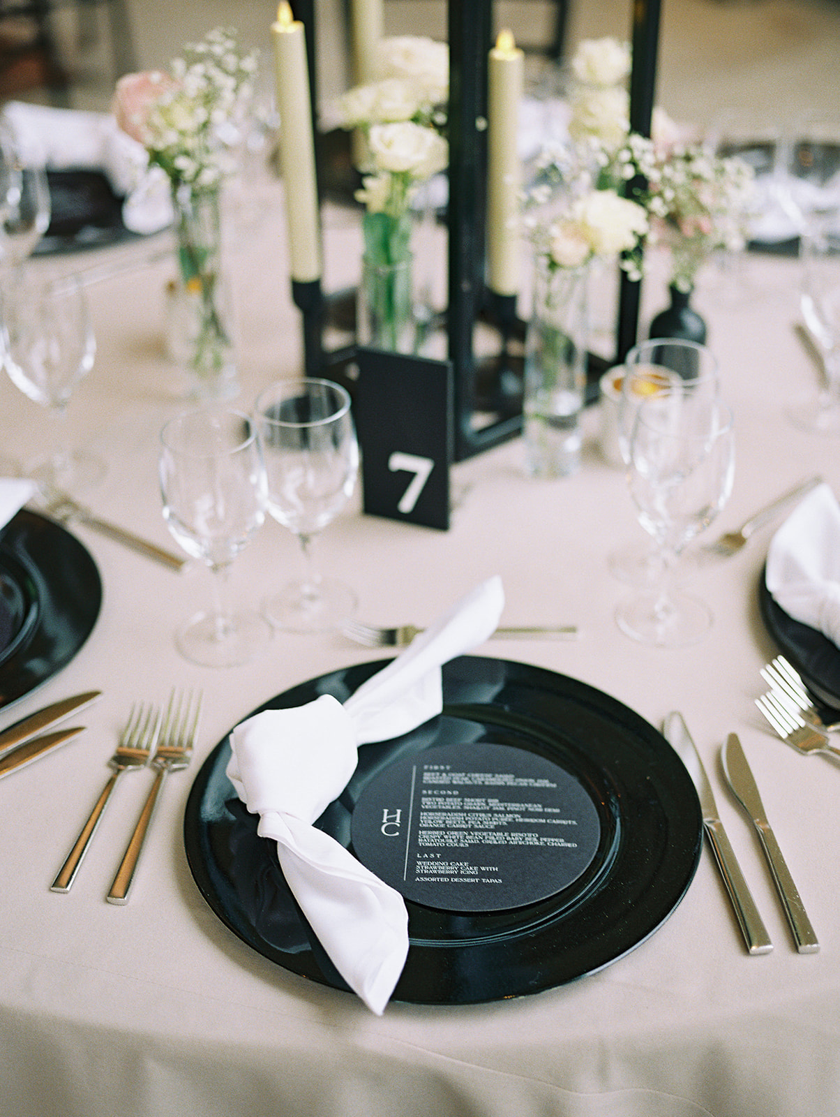 wedding tablescape with a closeup of black chargers and circular custom dinner menu