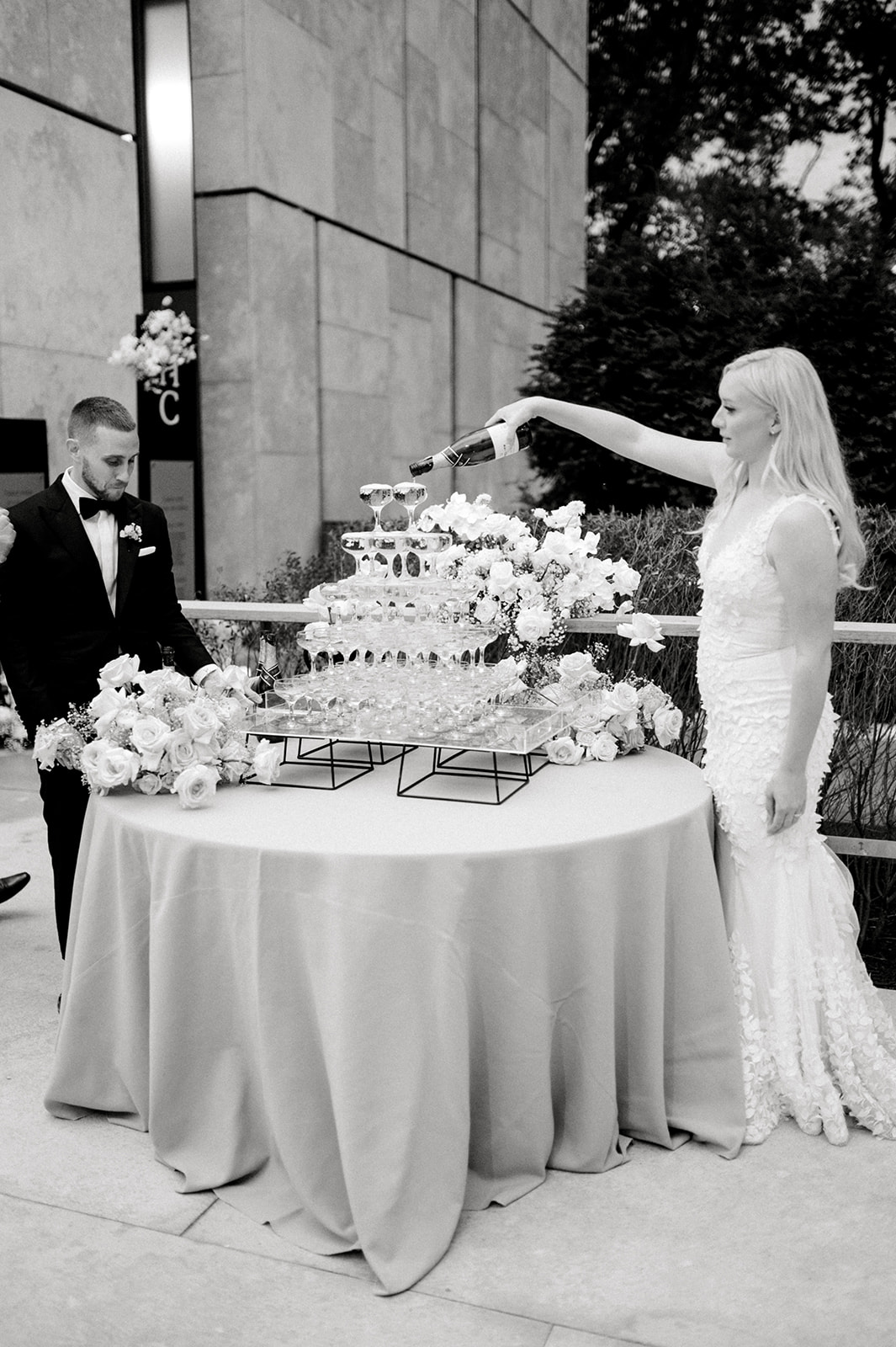 black and white photo of bride and groom pouring champagne into champagne tower