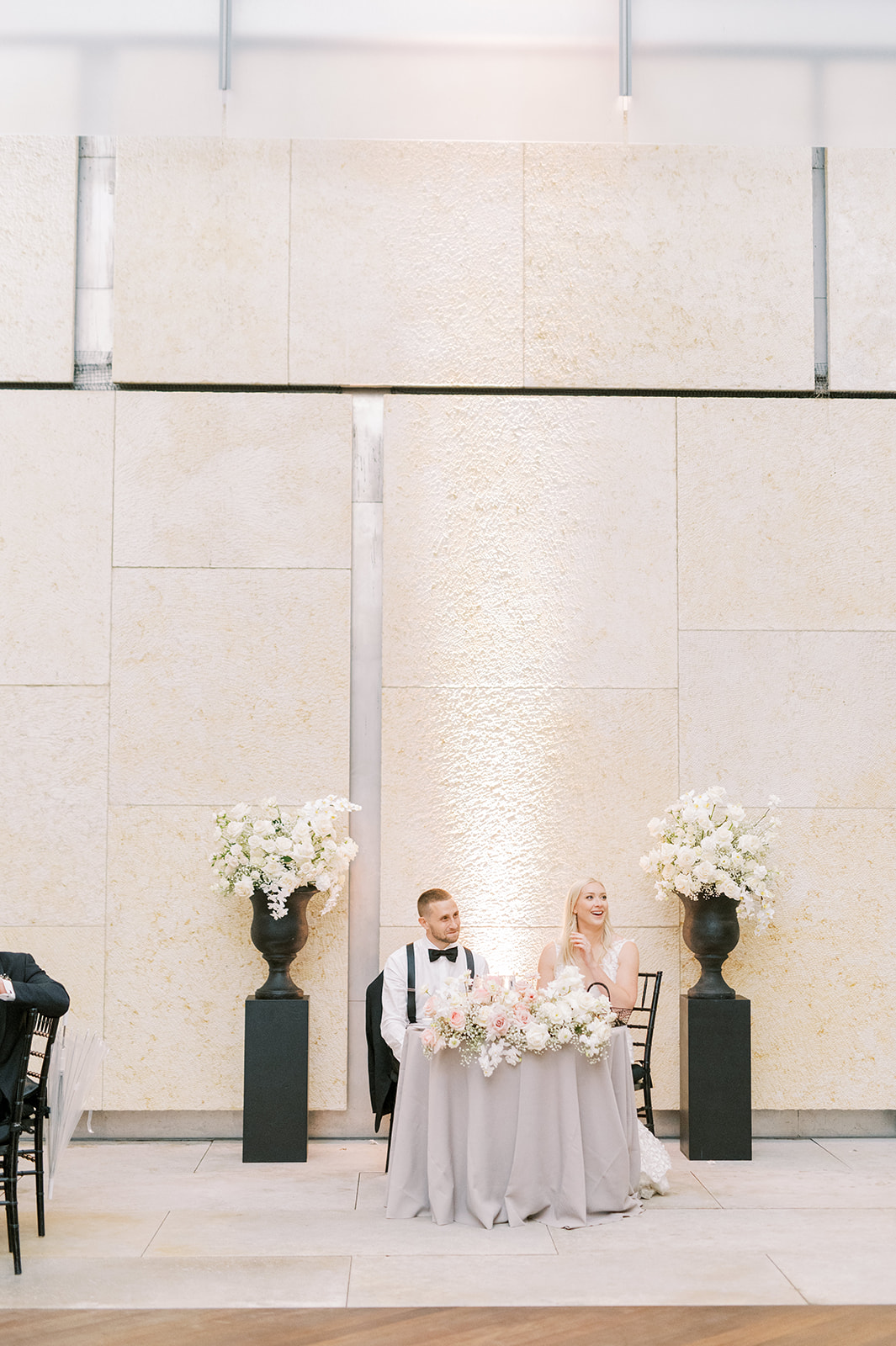 bride and groom sitting at swetheart table at the Barnes Foundation with black pedestals and urns with white florals