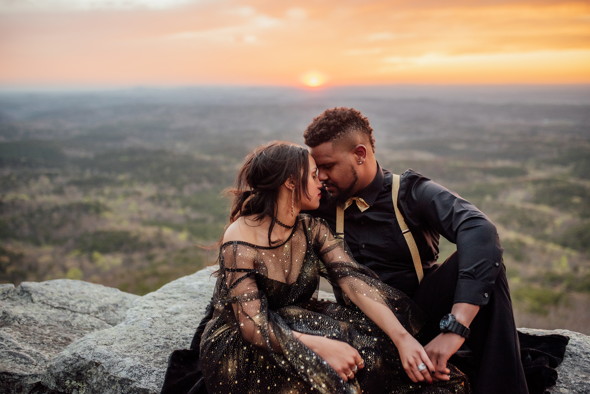 elopement couple with foreheads together sitting on a cliff with sunset behind.