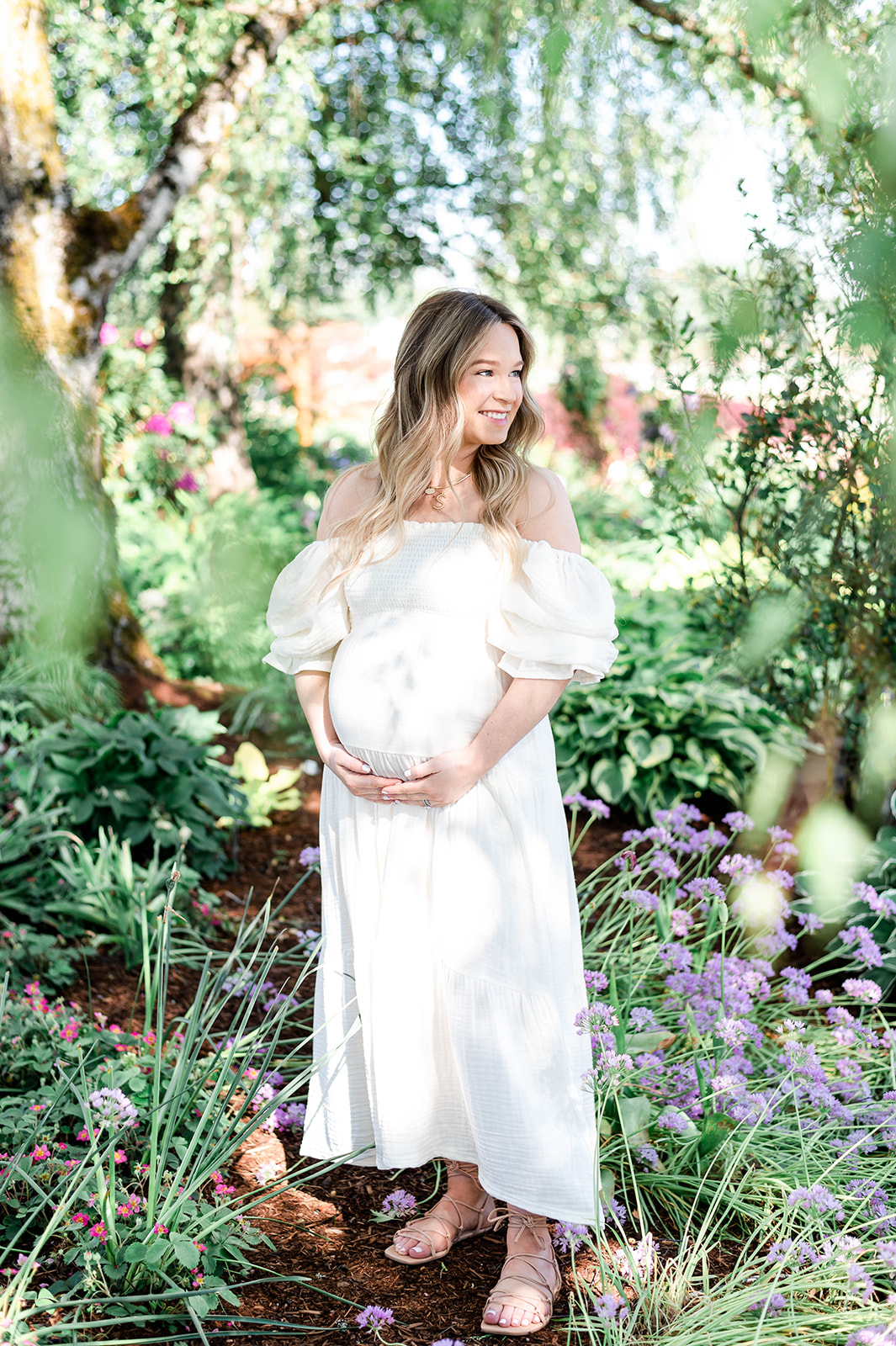 mother-to-be holding her baby bump, surrounded by lush greenery at Adelman Peony Gardens
 