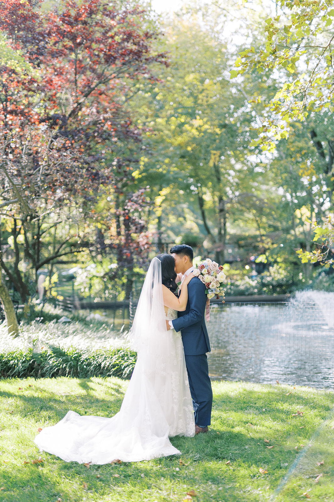 bride and groom embrace in on lawn in front of lake on sunny day at pomme in radnor, pa