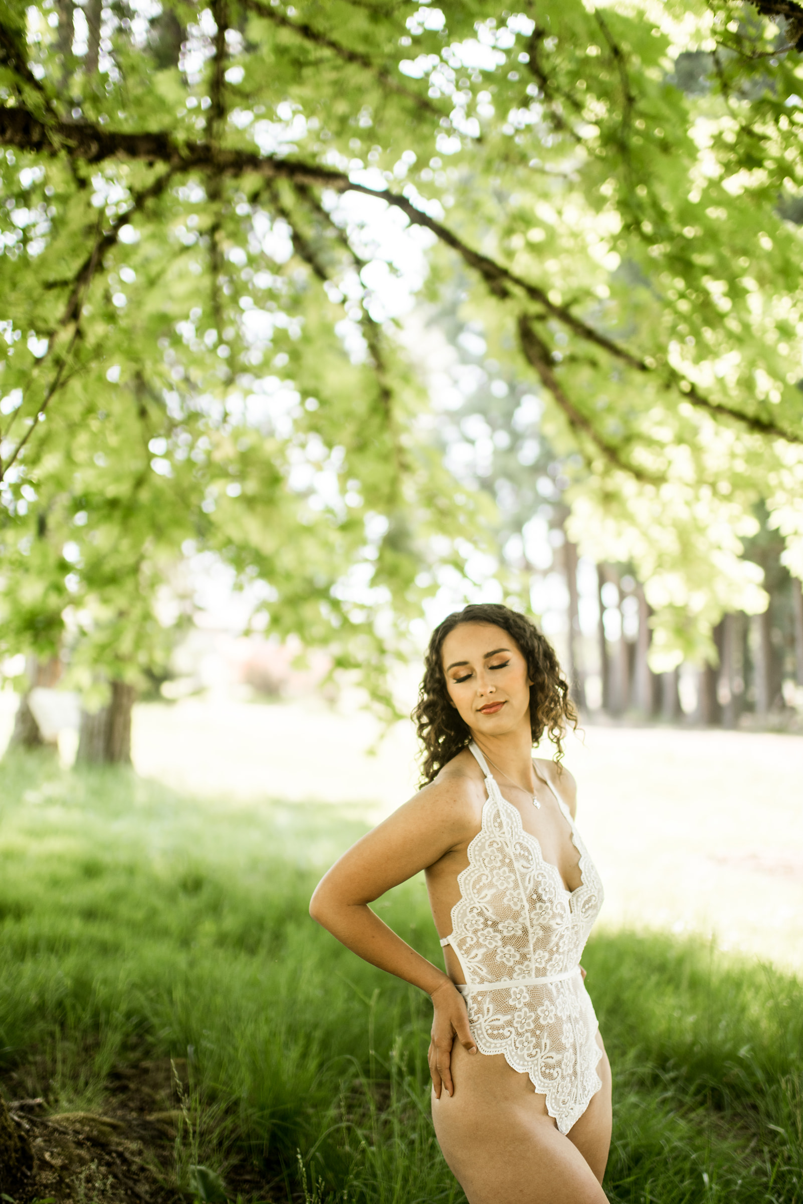 woman with curly hair poses underneath maple tree in lingerie for her boudoir session.