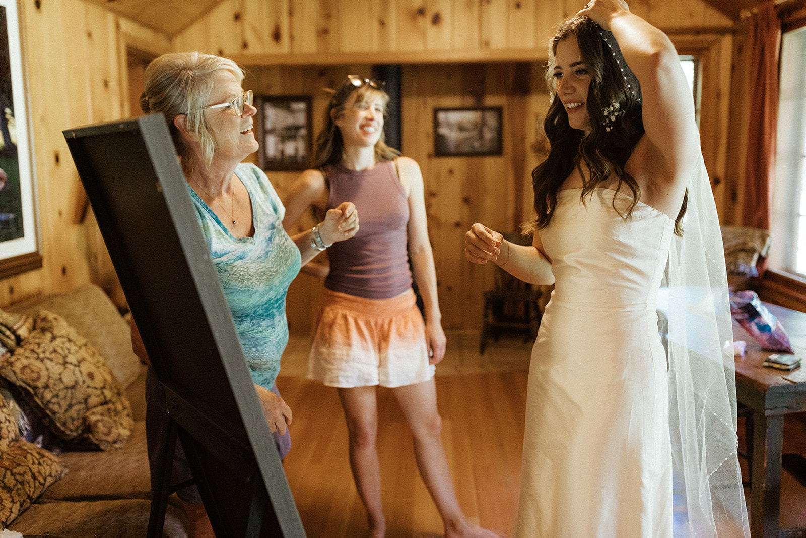 bride putting on veil with sister and mom beside her