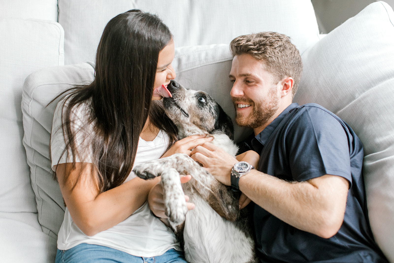 Couple cuddles on couch with their dog during their at-home engagement photoshoot 