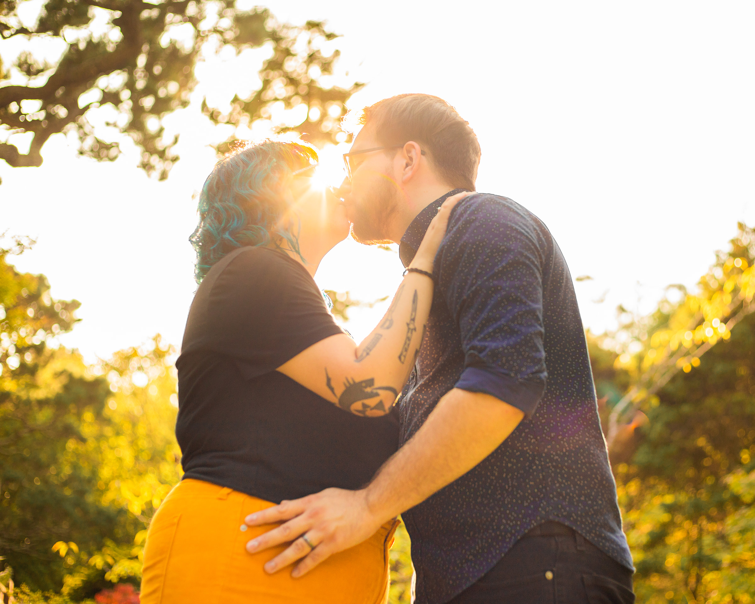 queer couple kiss with golden sun streaming behind them