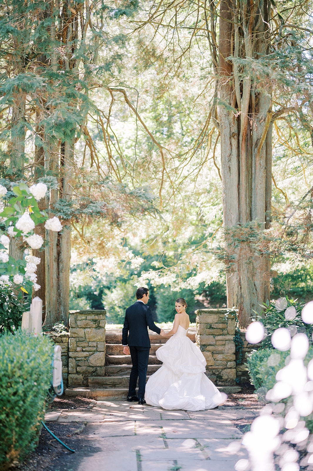 bride and groom walk amongst the tall trees for their Timeless Summer Wedding at Parque at Historic Hunting Hill Mansion