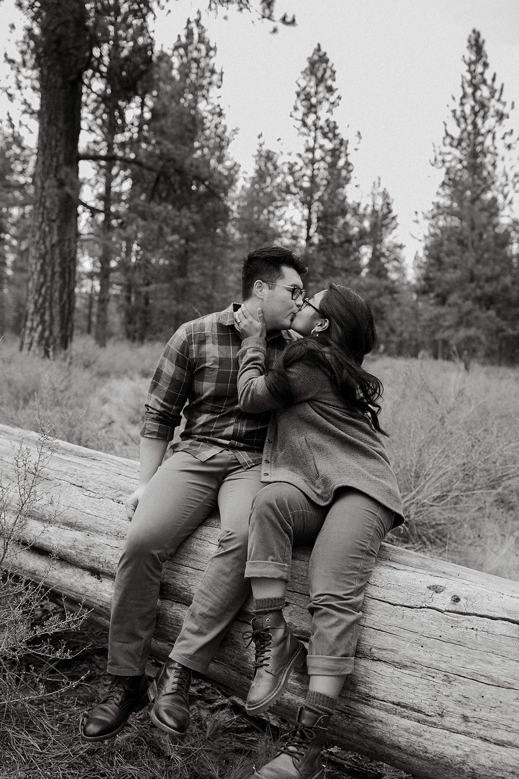 Bacl and white photo of a couple in the forest at Dillon Falls sitting on a log and embracing for a kiss.