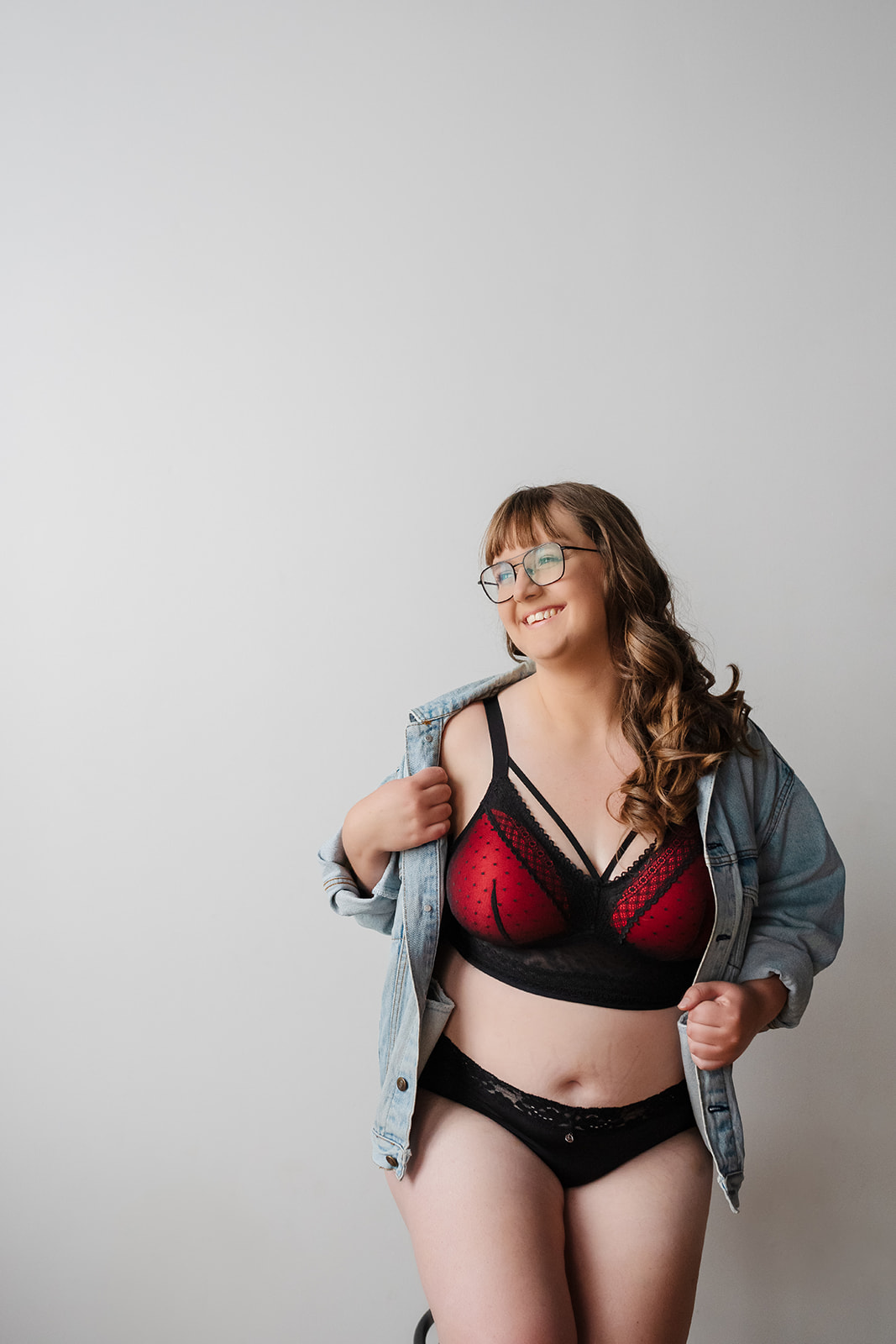 A woman wearing black and red bra and panty set with denim jacket during her boudoir photo session