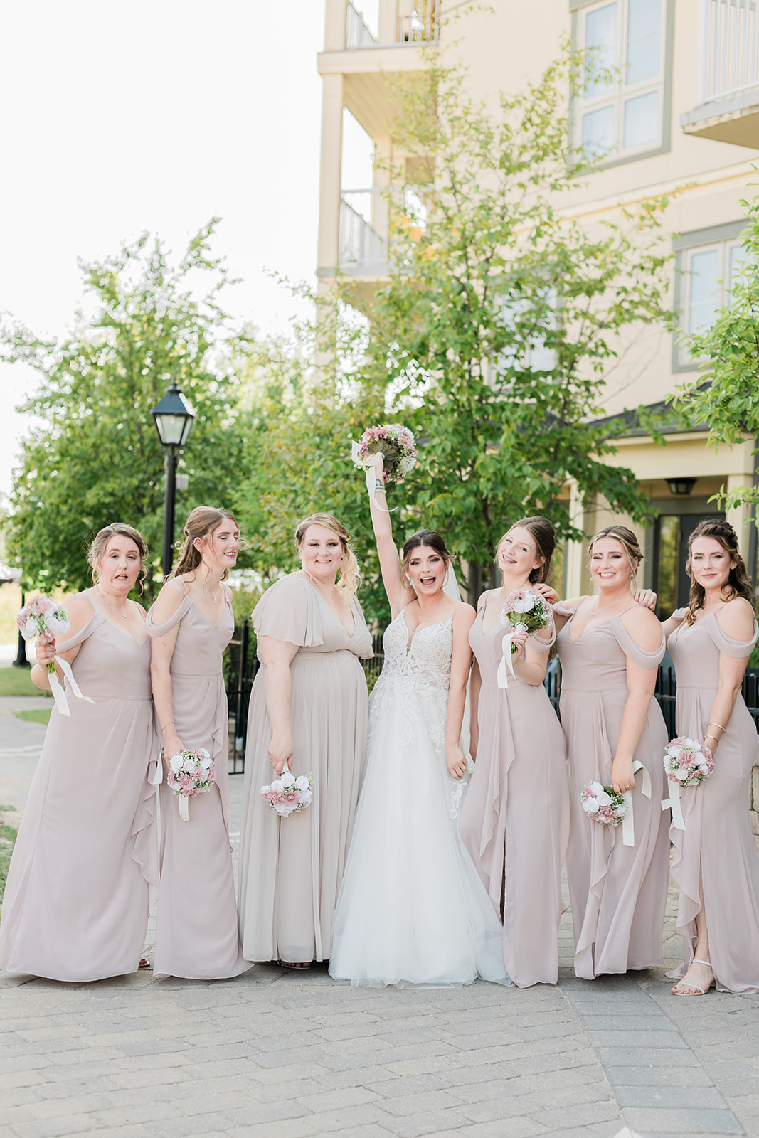 bride with arm up holding bouquet with bridesmaids 