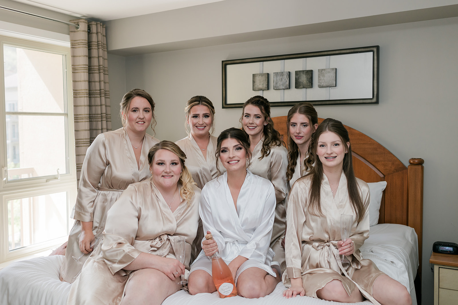 bride and bridesmaids sitting on bed in robes popping champagne
