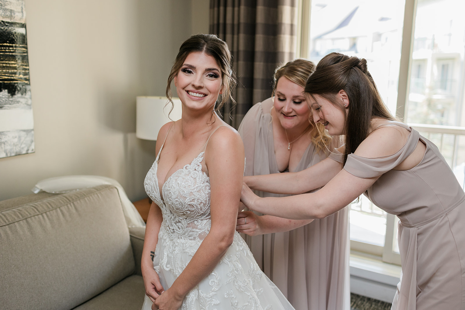 bridesmaids and bride smiling while getting dressed