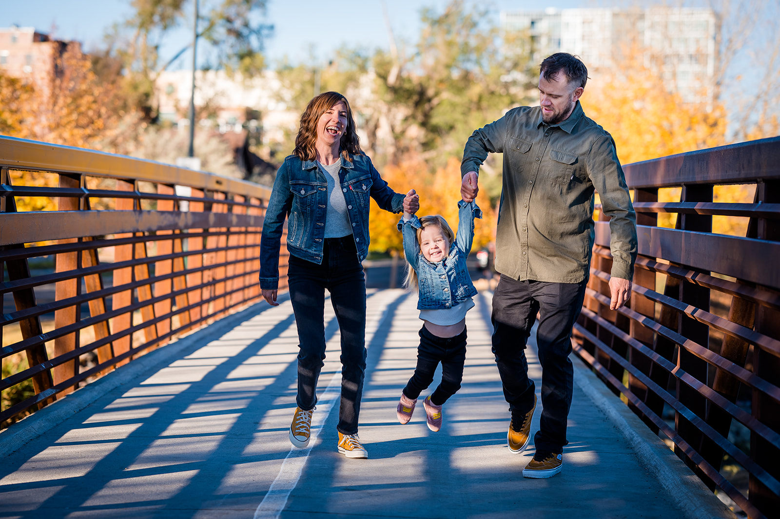 a family swings their little girl as they walk on a bridge in Denver