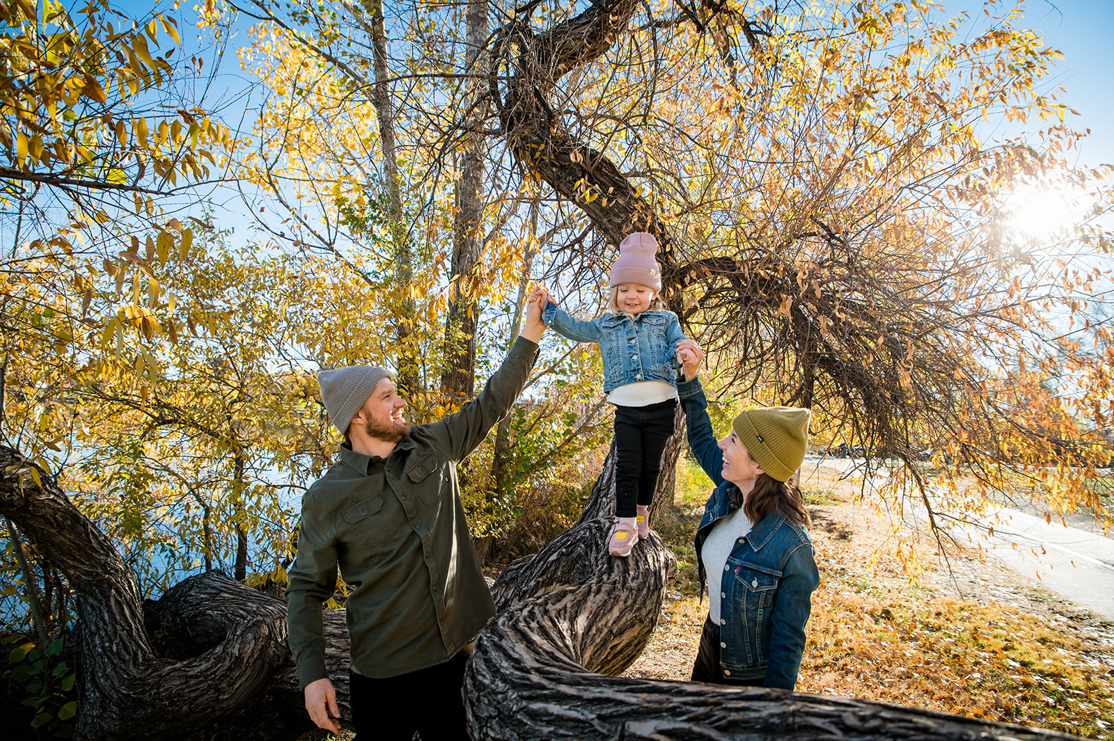 a mom and dad walk their child down a tree branch in the park near Sloane's Lake in Denver