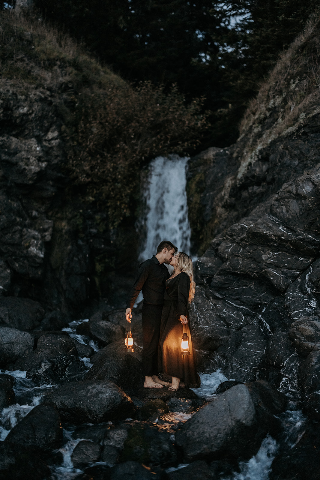 An eloping couple wearing all black kissing in front of a waterfall at Secret Beach in Southern Oregon.