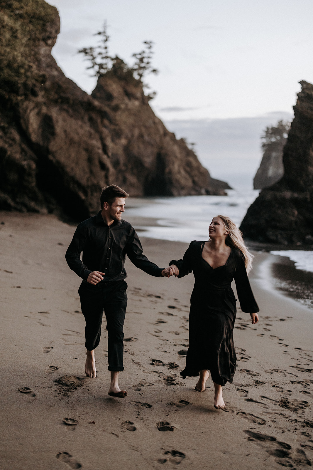 A couple wearing all black running on their elopement day at Secret Beach in Southern Oregon.