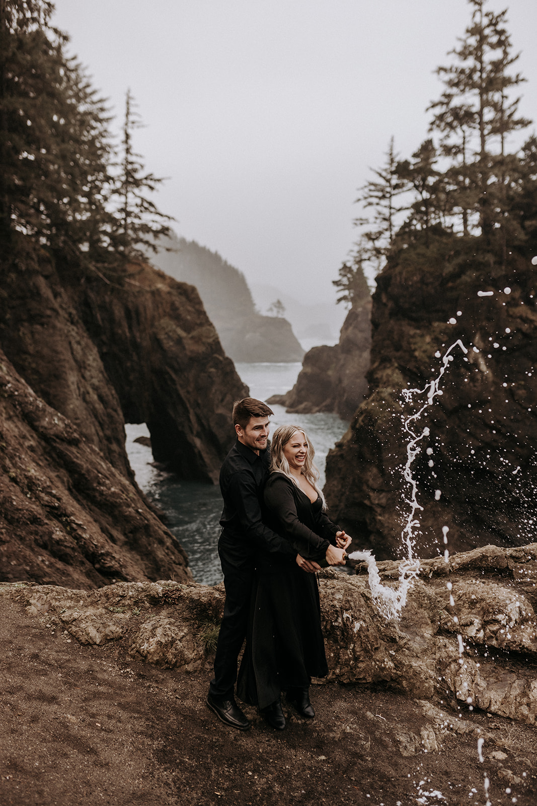 An elopement couple wearing all black spraying champagne on the Southern Oregon coast.