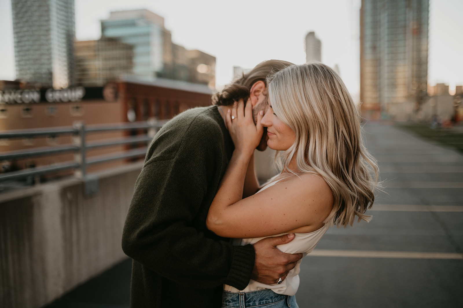 Blonde girl and brunette guy cuddling in close for their engagement photos on a rooftop in Calgary Alberta