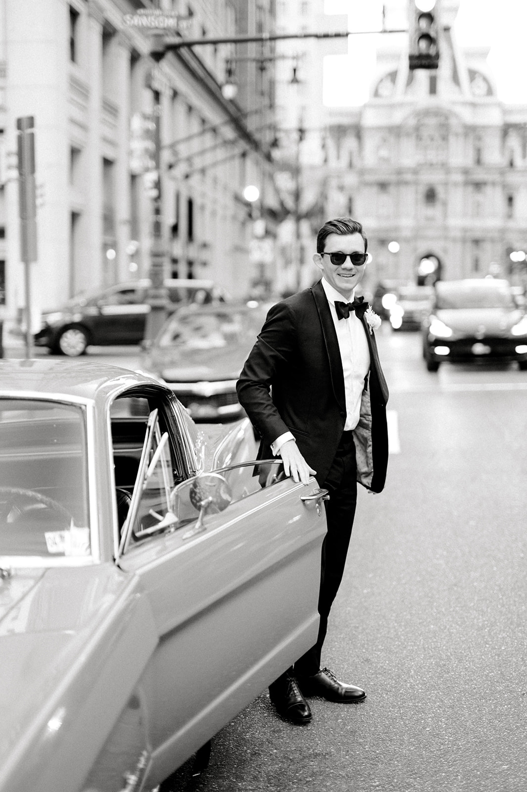 black and white photo of stylish groom exiting classic red mustang for union league of philadelphia wedding day