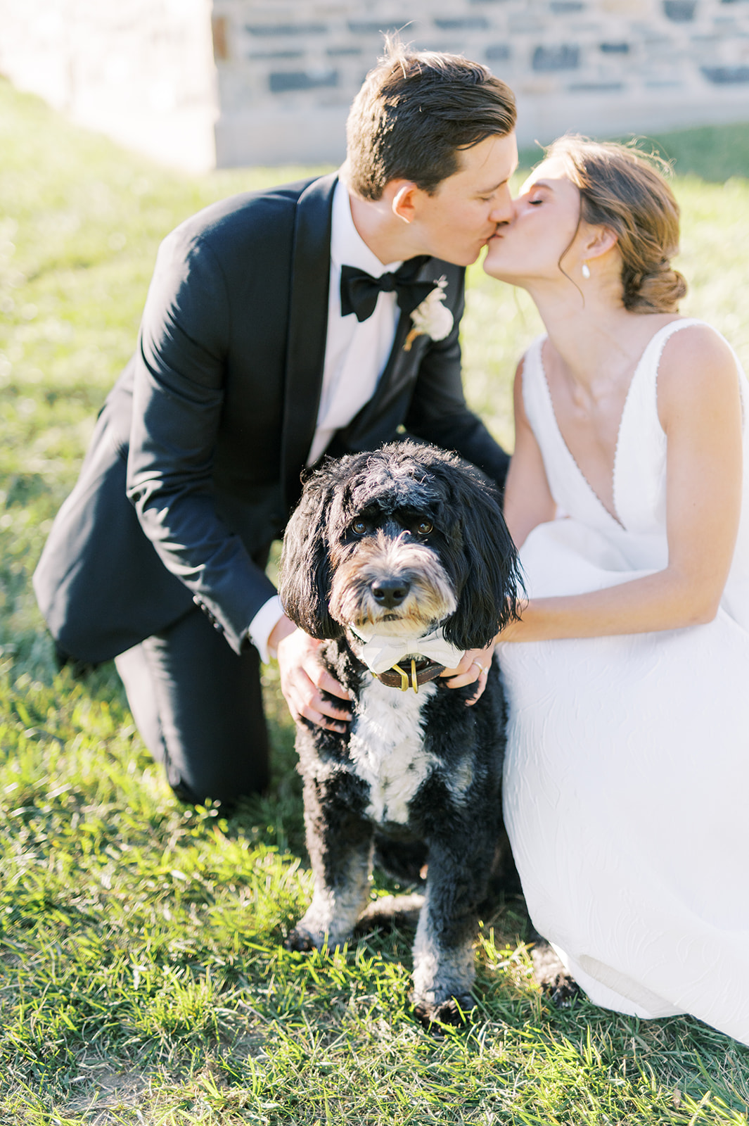 bride and groom kiss in the sun with their dog in front of Villanova for autumn wedding day