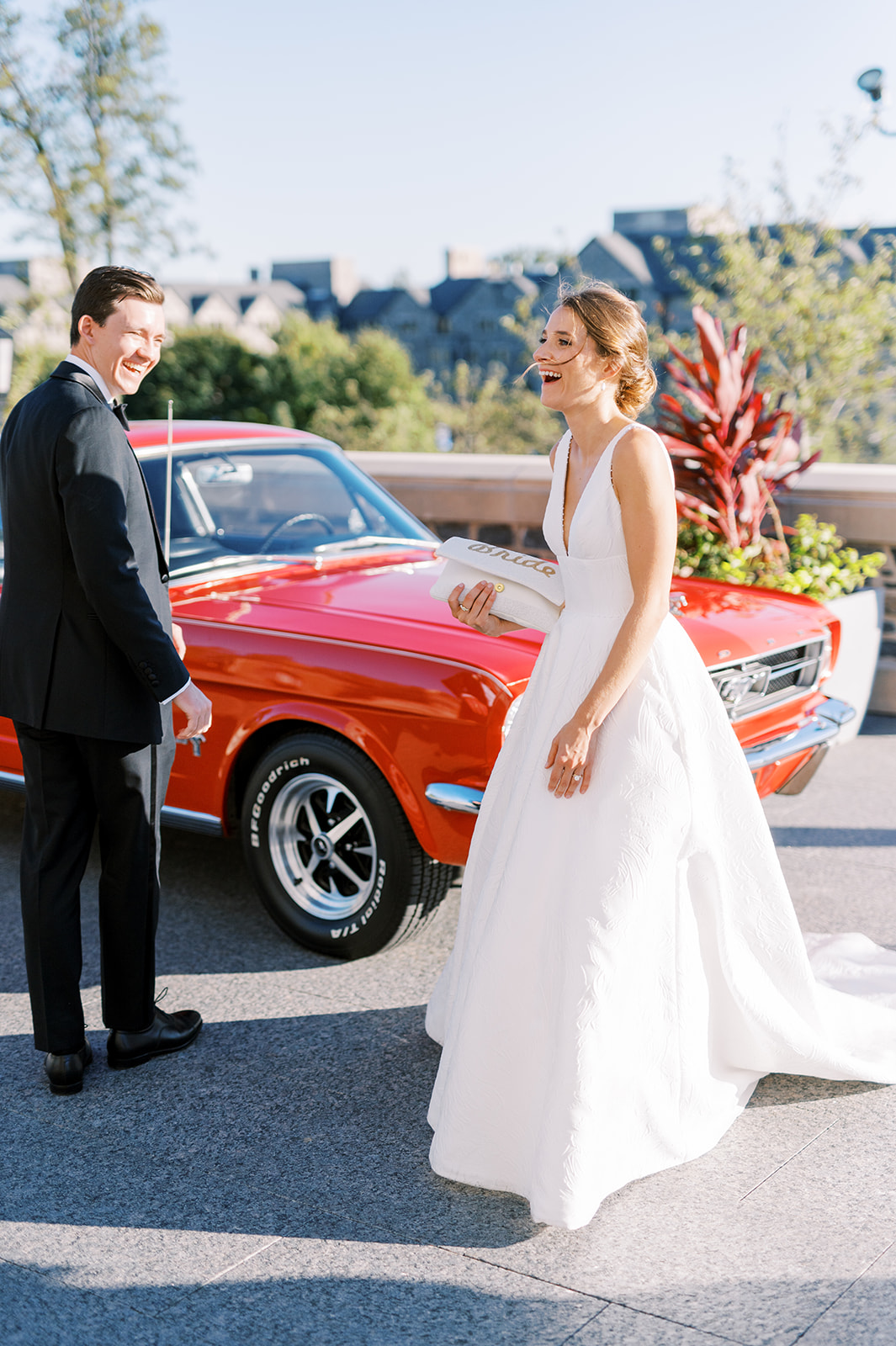 bride and groom laugh in front of classic red mustang for sunny villanova wedding day