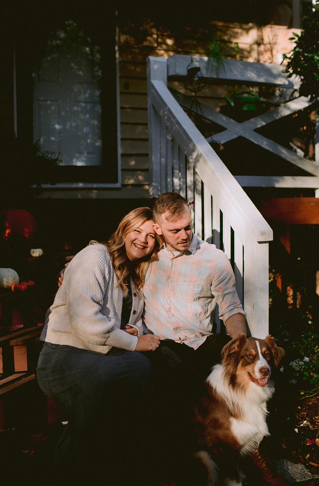 A preganant couple on their front porch with dog.