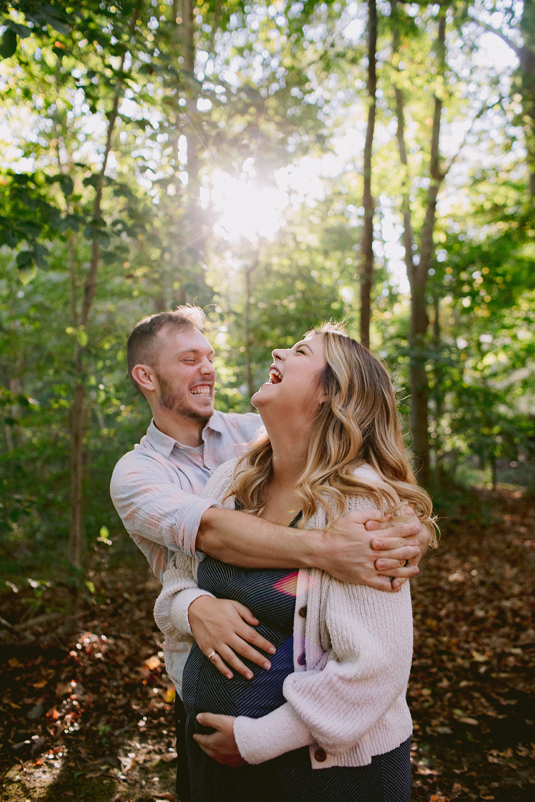 A preganant couple laughing in the woods near their home.A preganant couple laughing in the woods near their home.