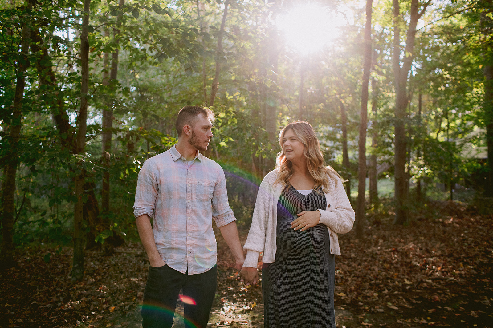 A preganant couple walking in the woods.