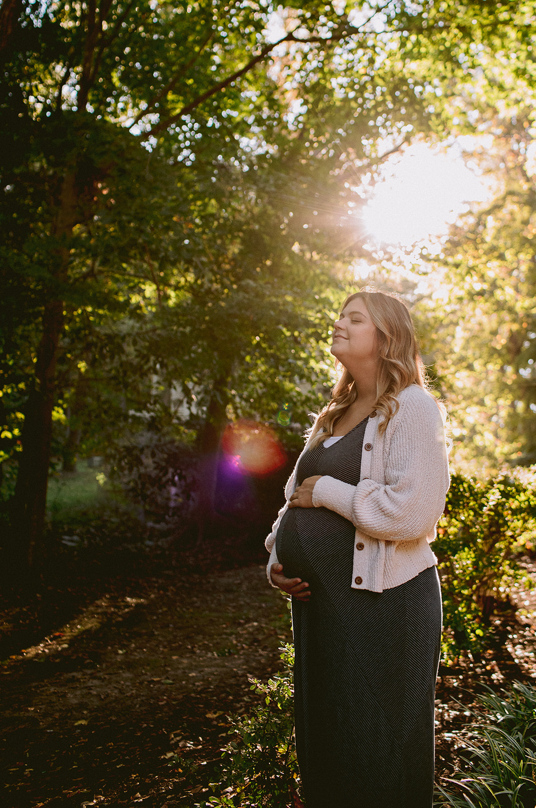 A preganant woman stands in warm afternoon sunlight.