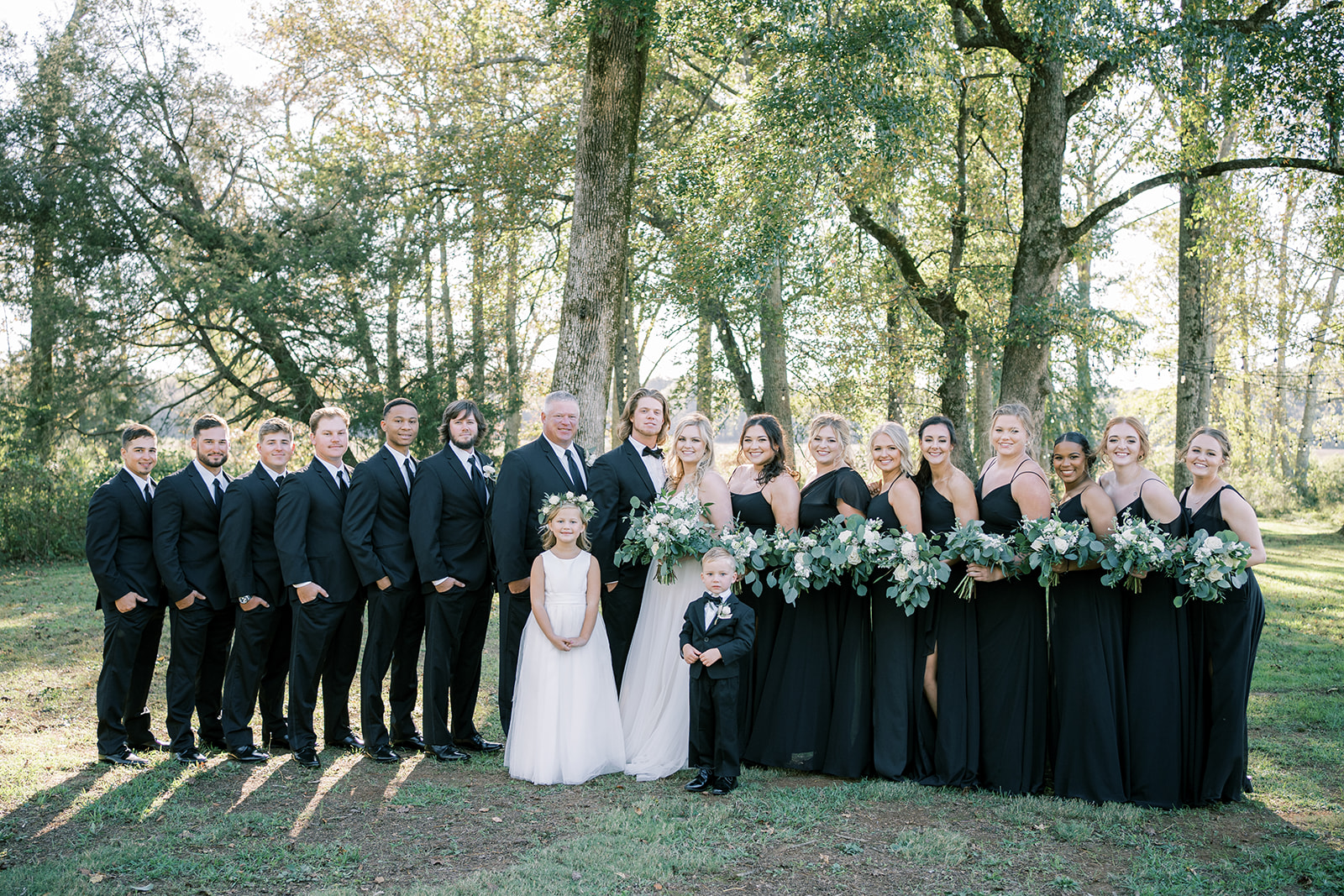 The wedding party stands together in all black for a fall wedding at Harvest Hollow in Toney, Alabama
