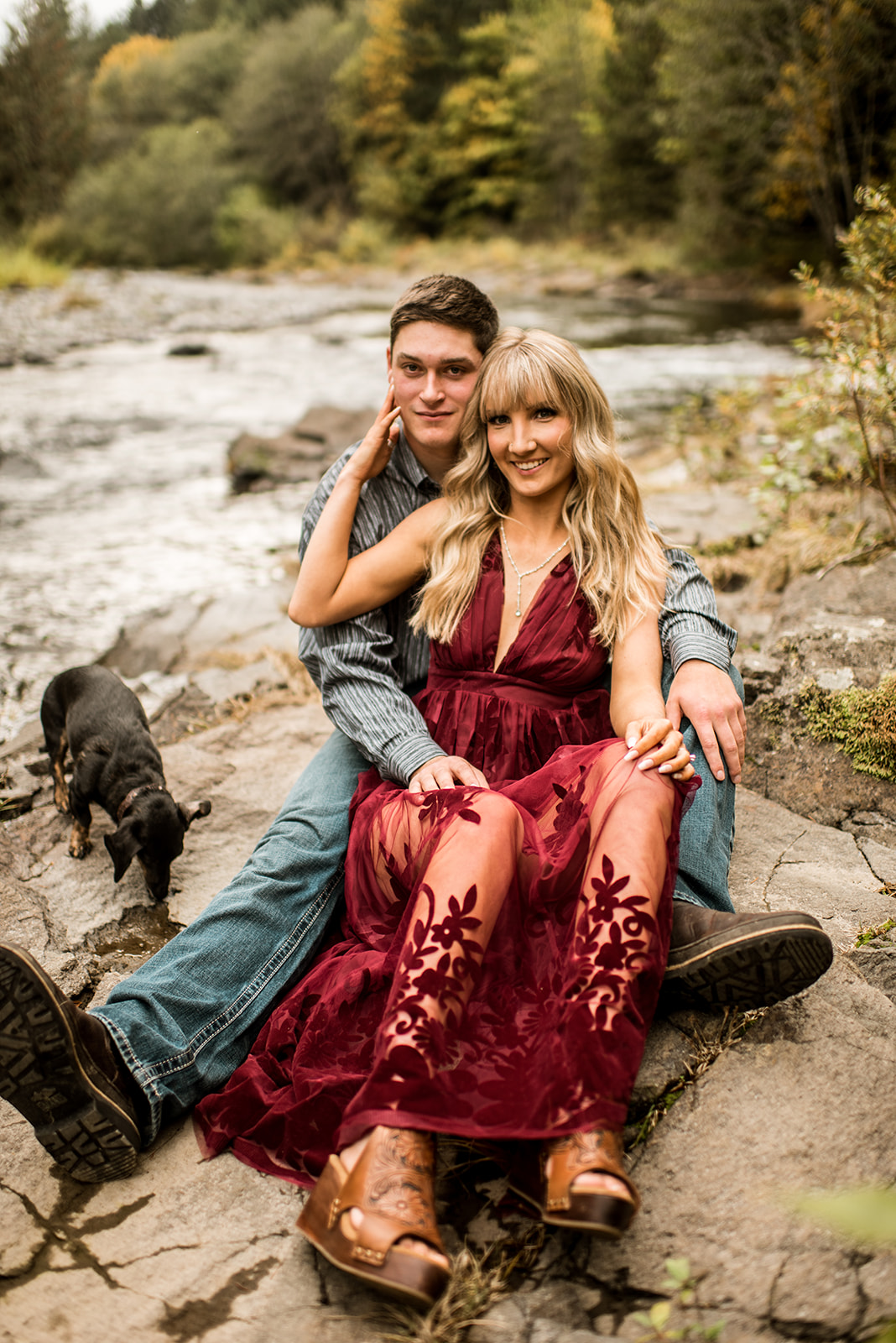 Engaged couple sits along rocks on the Molalla River for their engagement portraits
