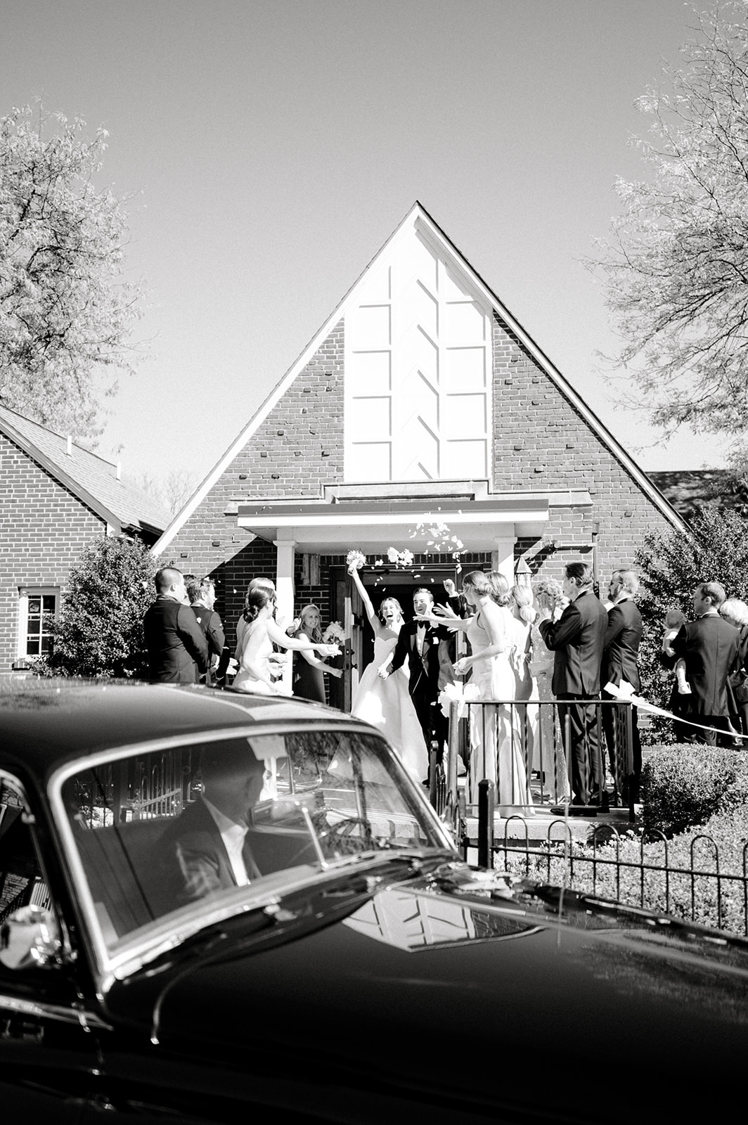 black and white photo of bride and groom cheering as exiting church with all guests