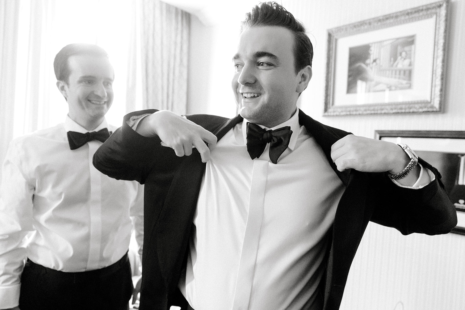 black and white photo of groom putting on his suit jacket