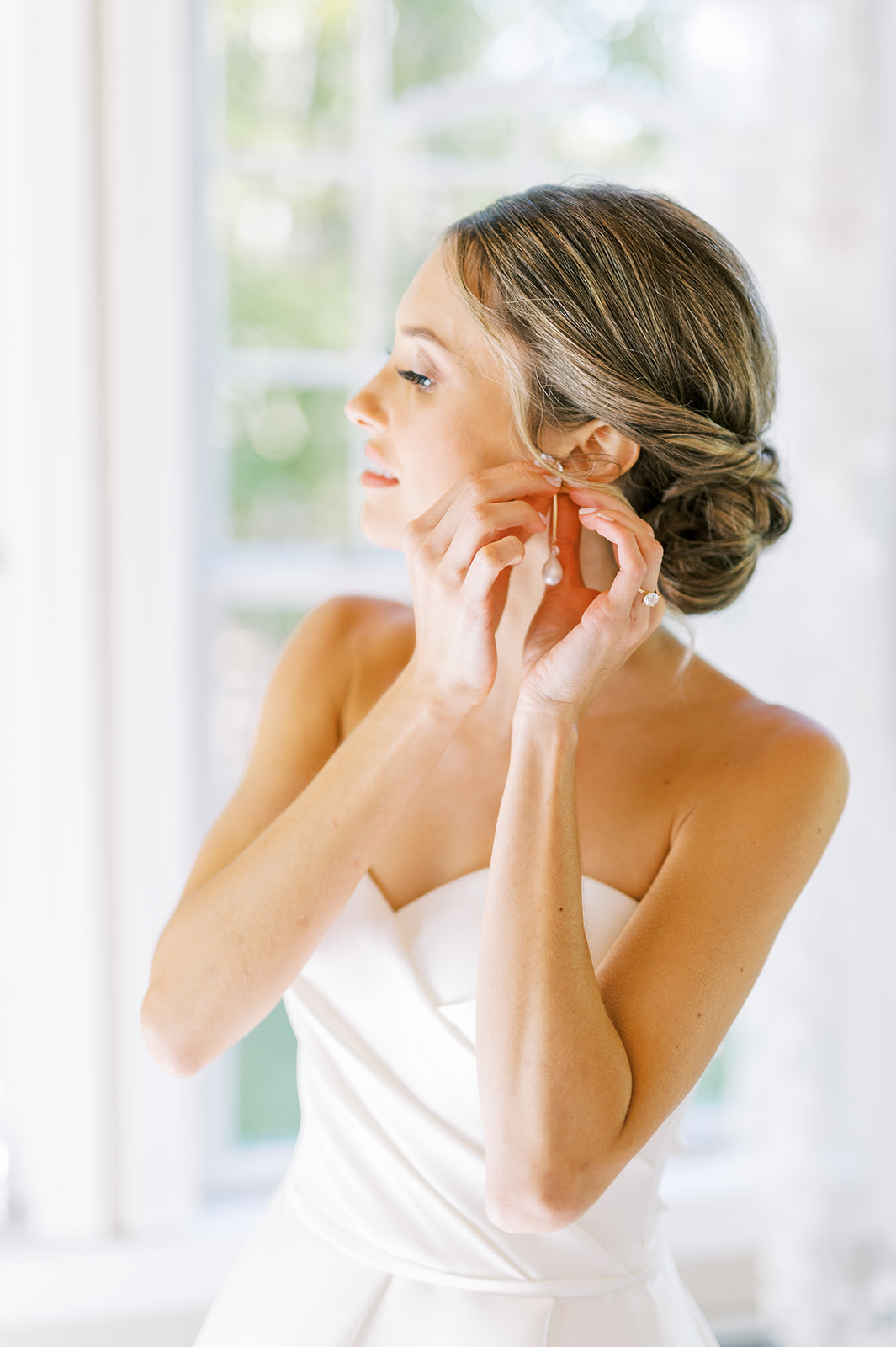 bride putting on earring in brightly lit space