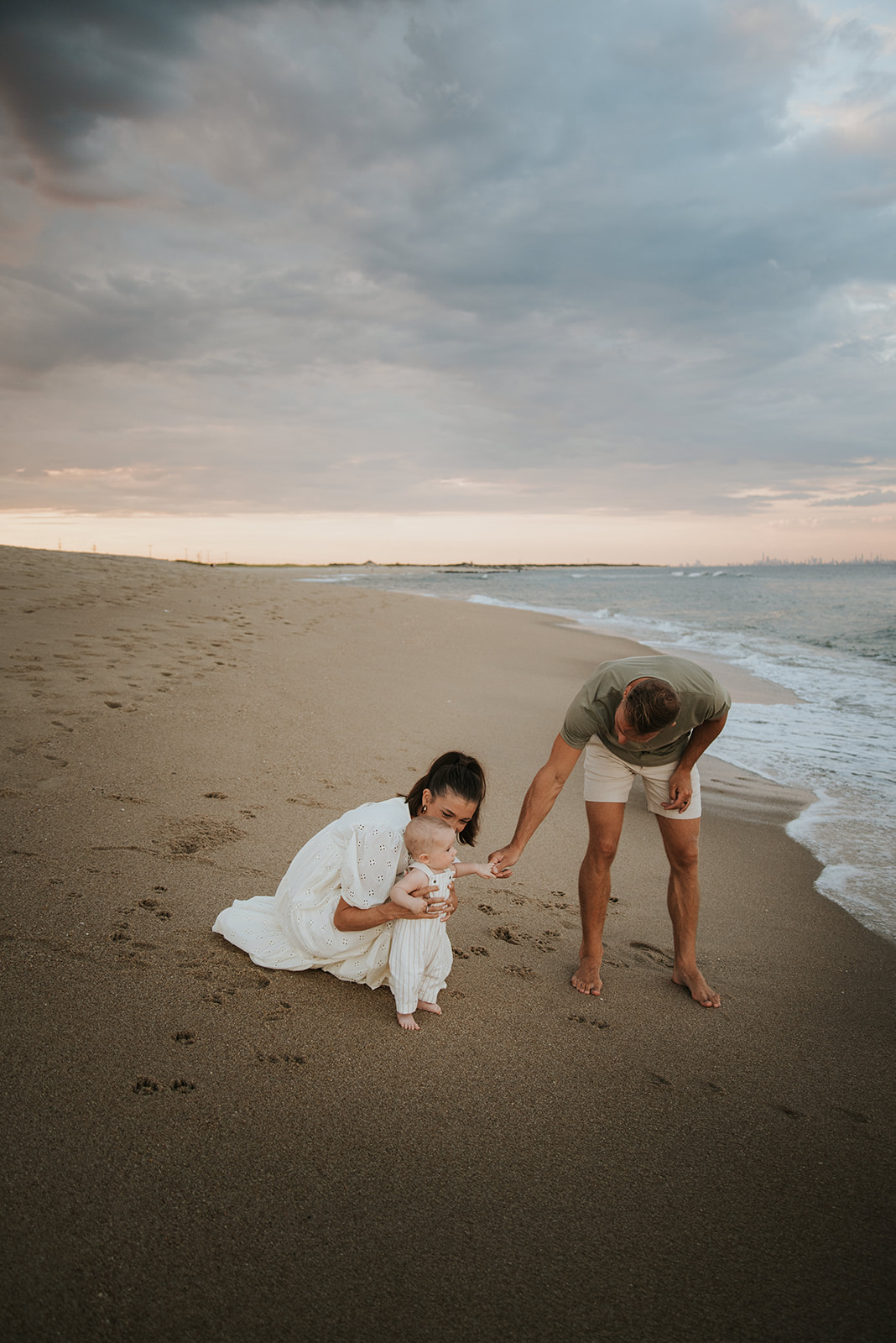 A family photoshoot at the beach with their 6 month old baby who is at the beach for the first time at sunset