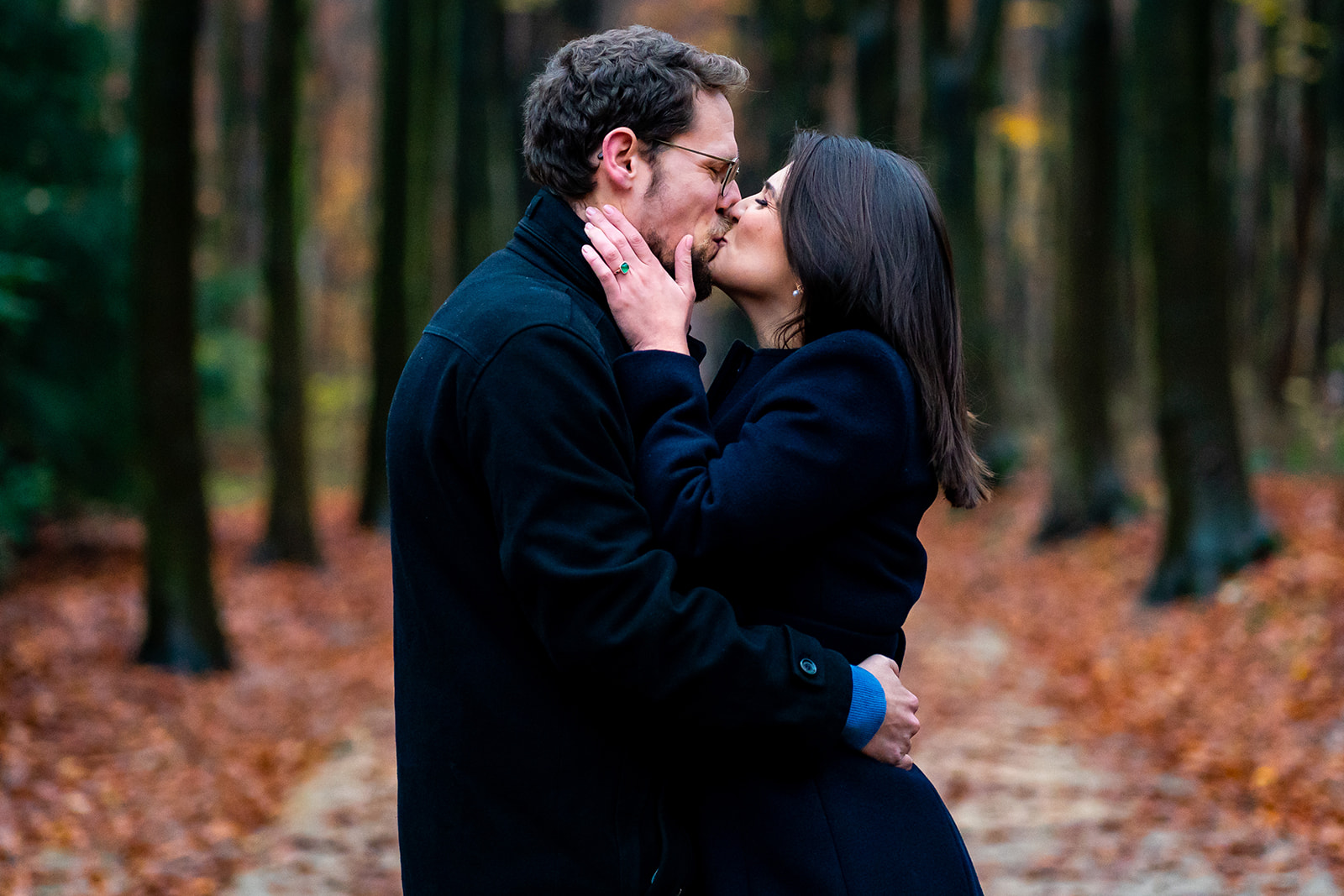 Deux amoureux s'embrassent sur un chemin du bois de la Cambre, entourée de couleurs d'automne lors d'une séance photo