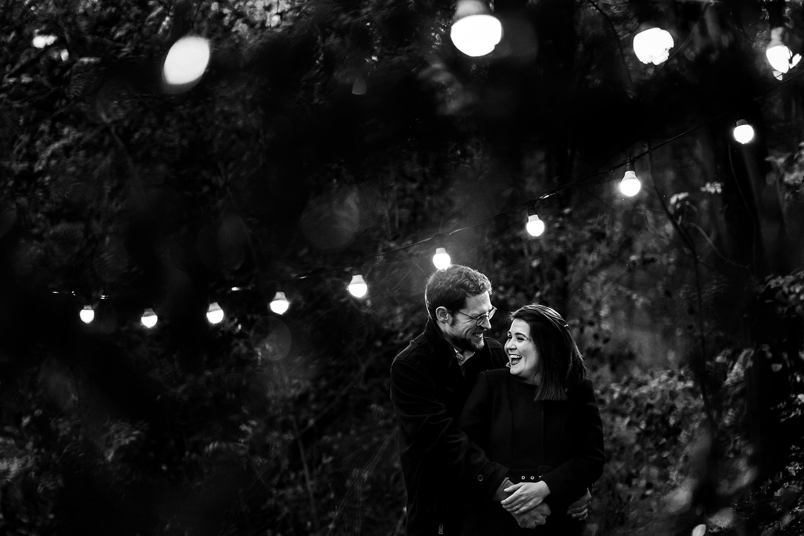 Deux amoureux, se tiennent sous des lampions, elle lui sourie amoureusement, lors d'une session photo couple à Bruxelles