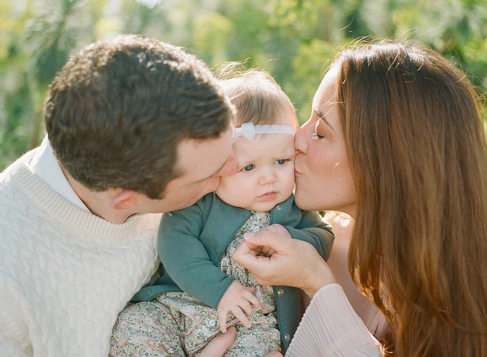 family photo of mom and dad kissing cheeks of three month old baby girl