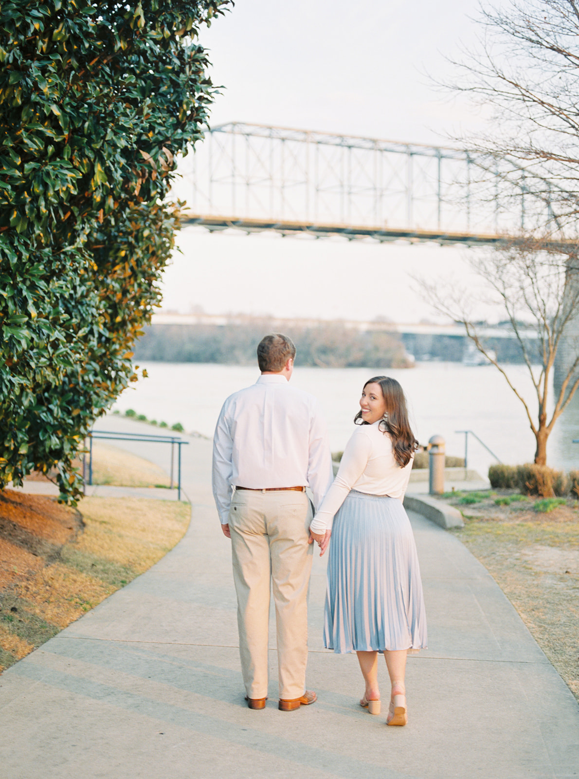A couple walks in front of the Walnut Street Bridge at Coolidge Park in Chattanooga, Tennessee