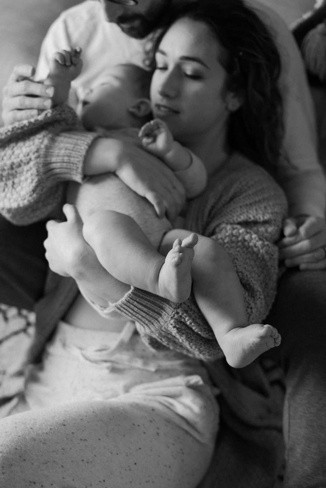 A tender black and white photo of mama and baby both being held by dad in their home. 