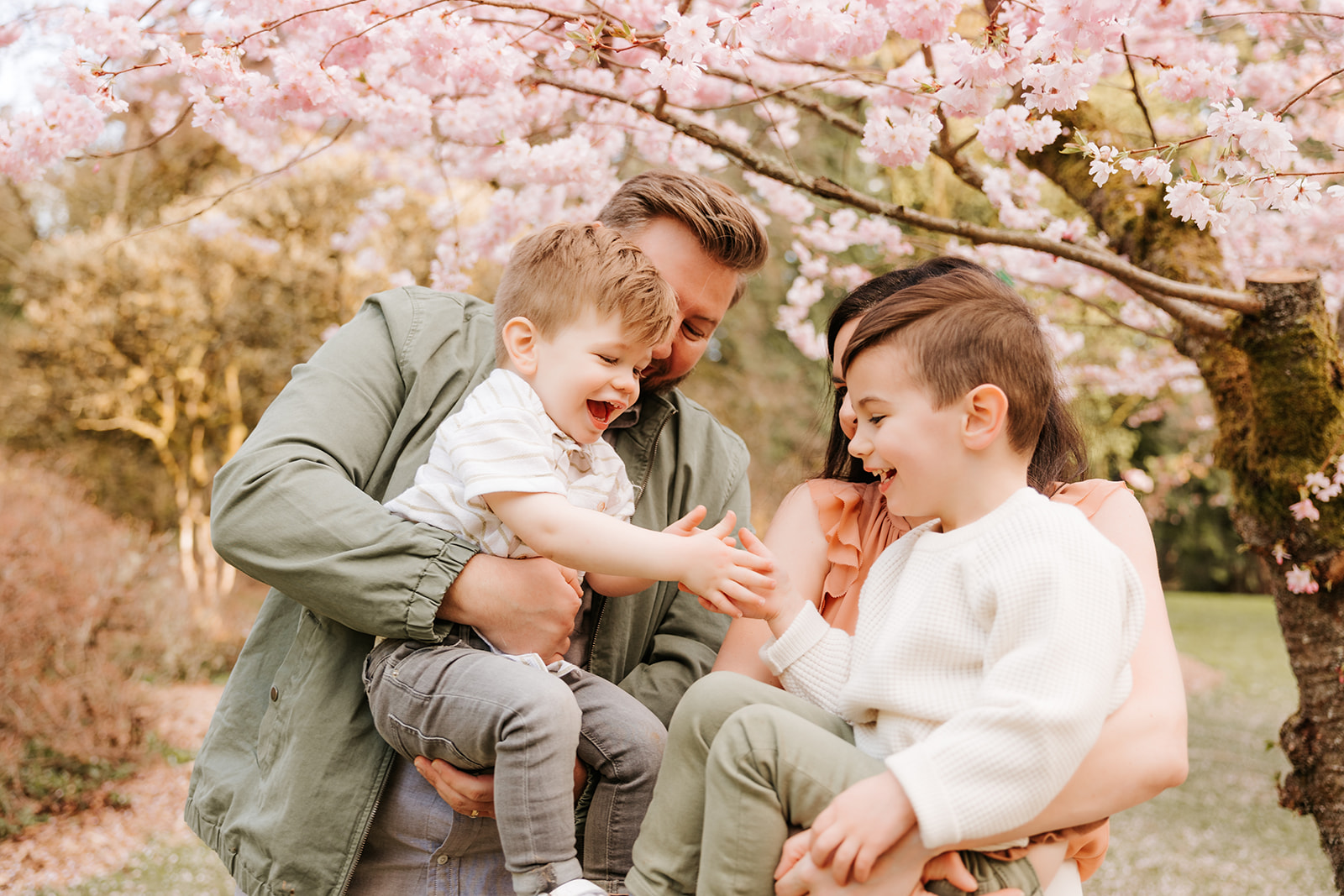 A close-up photo of a family of four laughing together in front of a cherry blossom tree. 