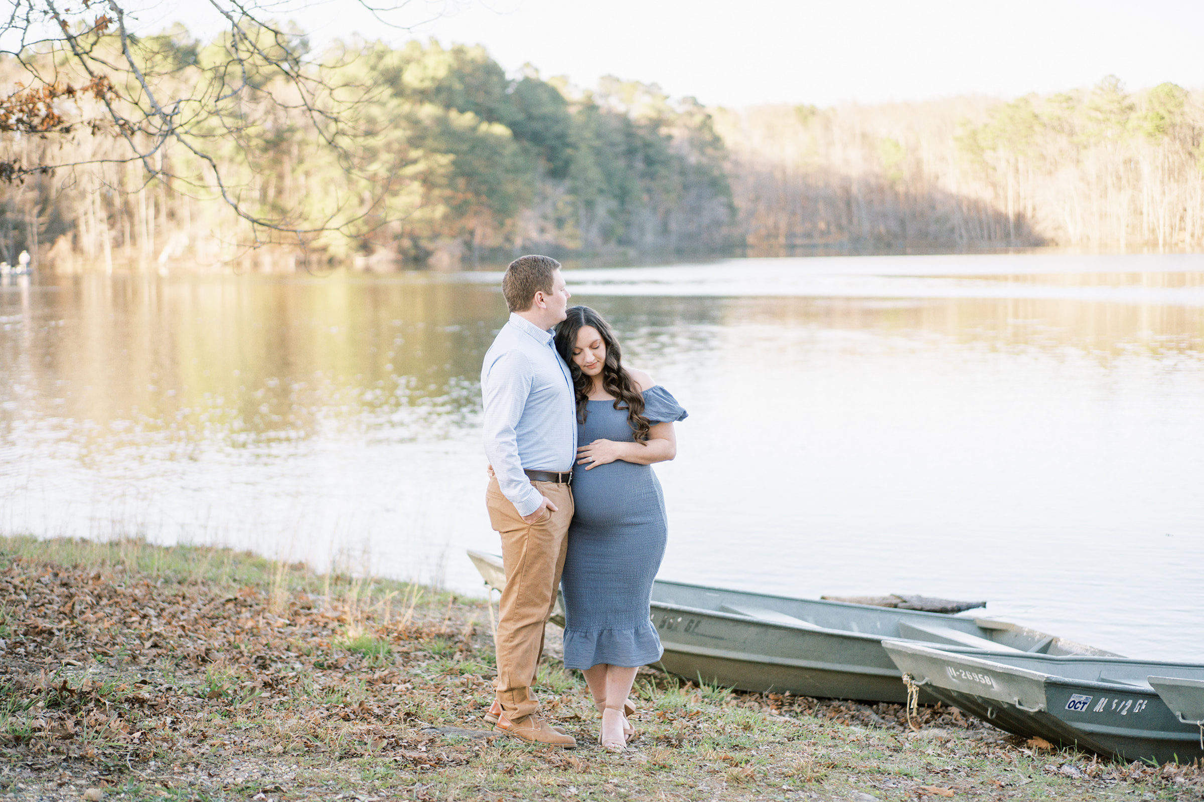 Husband and wife embrace in front of DeKalb County Lake during intimate maternity photography session